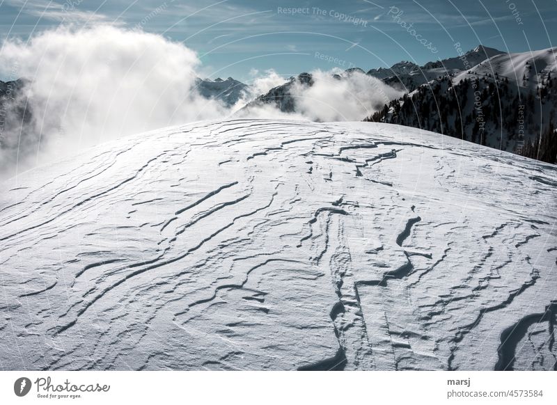 Vom Wind geformte Schneedecke. Im Hintergrund schneebedeckte Gipfel und aufsteigender Nebel. Winter einzigartig Alpen Schneelandschaft Schneefeld Natur