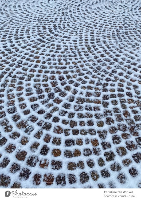 Leicht verschneites Kopfsteinpflaster. Schnee liegt in den Fugen und betont die bogenförmige Anordnung der Steine Pflastersteine Glätte Winter Muster