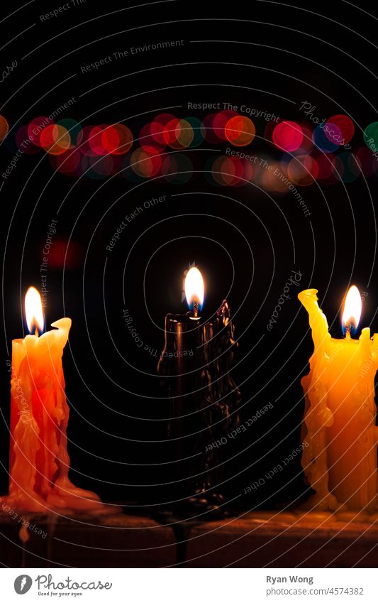 Nahaufnahme von drei brennenden farbigen Kerzen mit einem Bokeh-Hintergrund in einer windigen Nacht. Gedenkstätte Erinnerungen Flamme Kerzenschein