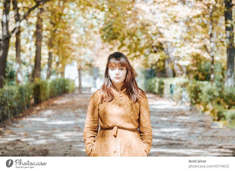 Herbst Porträt einer jungen Frau mit einem Hipster Kleid Spaziergänge im Park mit Laub. Platz für Text, Copy Space. Herbstlicher Park. Blick ernst in die Kamera