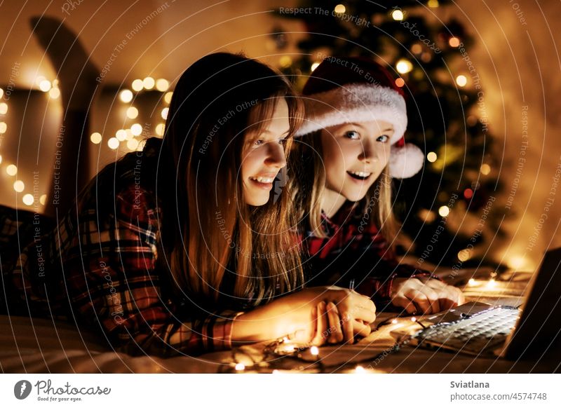 Zwei charmante Schwestern liegen an Weihnachten oder Silvester mit einem Laptop auf dem Bett und gratulieren ihren Freunden und Verwandten online. Weihnachtsgrüße online, virtuelle Party zu Weihnachten