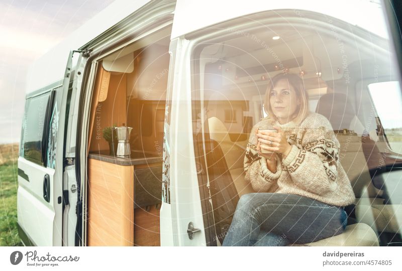 Frau mit einer Tasse auf dem Vordersitz eines Wohnmobils Sitzen Kleintransporter kalt wärmende Hände Kaffee Sonnenlicht Morgendämmerung Textfreiraum