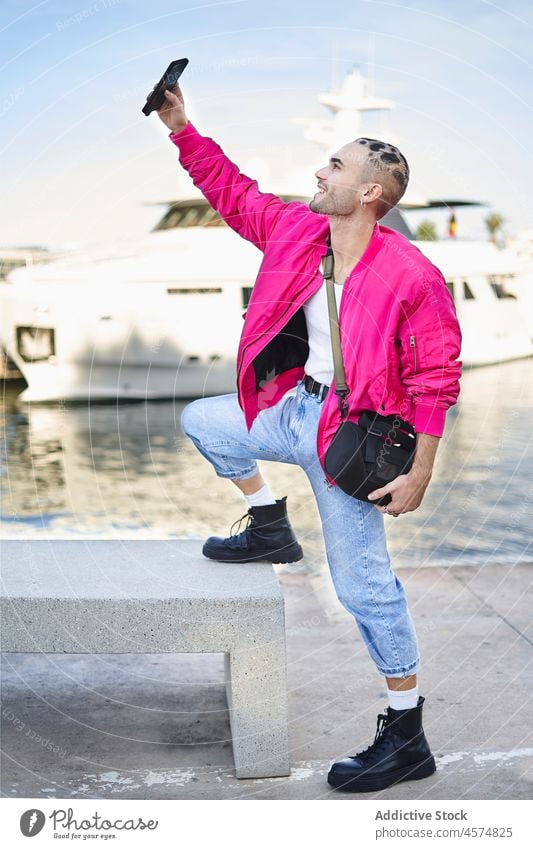Lächelnder stilvoller Mann, der ein Selfie mit seinem Smartphone auf dem Deich macht informell Stil Selbstportrait benutzend Jachthafen trendy positiv Pier cool
