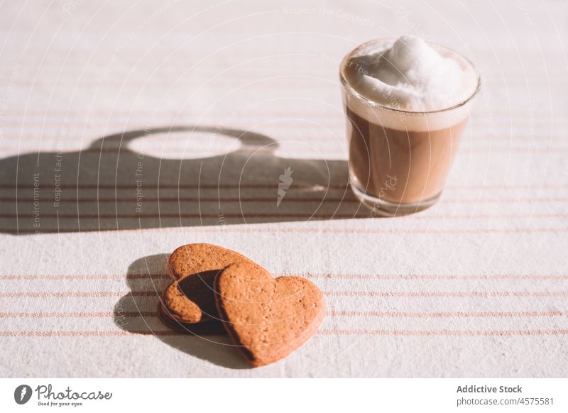 Glas schaumiger Kaffee mit herzförmigen Keksen auf dem Tisch serviert Latte Macchiato Dessert trinken Herz lecker geschmackvoll süß schäumen Form dienen