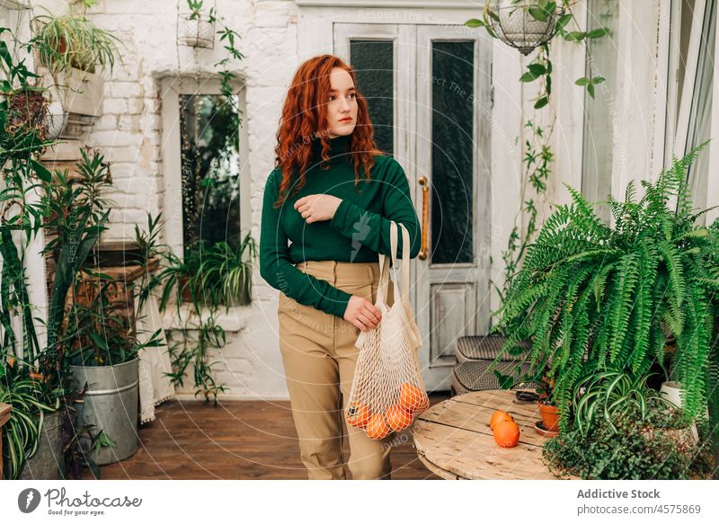 Frau mit wiederverwendbarer Schnurtüte mit Mandarinen im Garten Einkaufsnetz keine Verschwendung Zimmerpflanze botanisch vegetieren Botanik kultivieren wachsen