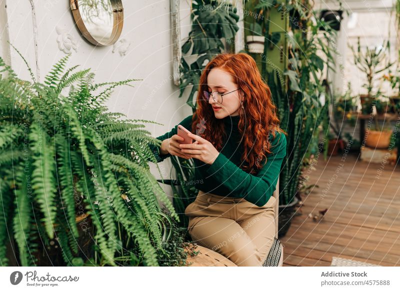 Positive rothaarige Frau benutzt ein Smartphone benutzend botanisch wachsen Pflanze Garten positiv Laubwerk Funktelefon Botanik eingetopft Selbstportrait