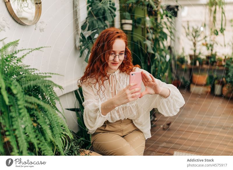 Positive rothaarige Frau macht Selfie mit Smartphone benutzend botanisch wachsen Pflanze Garten positiv Laubwerk Funktelefon Botanik eingetopft Selbstportrait