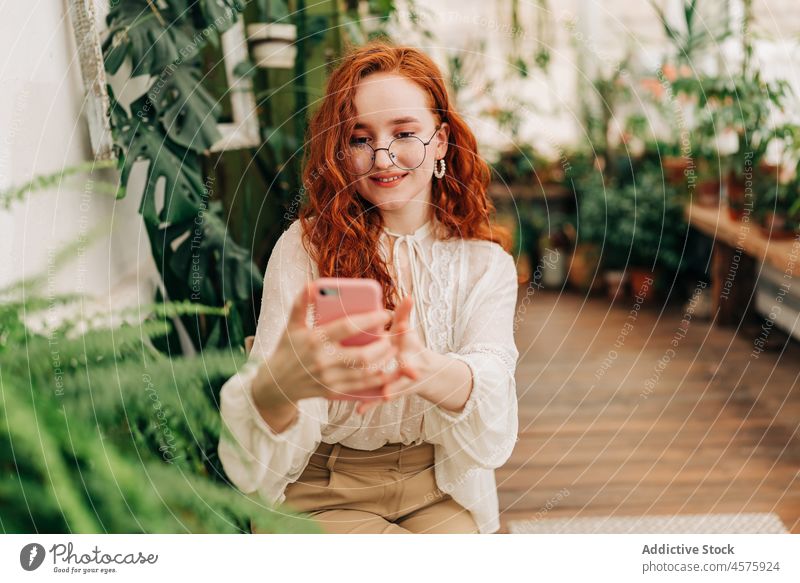 Positive rothaarige Frau macht Selfie mit Smartphone benutzend botanisch wachsen Pflanze Garten positiv Laubwerk Funktelefon Botanik eingetopft Selbstportrait