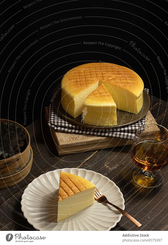 Japanischer Käsekuchen mit Getränk auf dem Tisch ganze Torte japanischer Käsekuchen Dessert trinken Lebensmittel halbdunkel Teller Glas Portion appetitlich