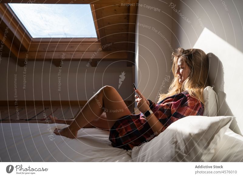 Frau benutzt Mobiltelefon auf dem Bett im Dachgeschoss Dachboden Garret benutzend Funktelefon Smartphone Browsen Kälte ruhen Komfort Apparatur