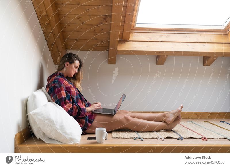 Fokussierte Dame mit Laptop auf dem Dachboden Frau Tippen benutzend Garret Bett Browsen ruhen Kälte Tee unabhängig Komfort Apparatur sich[Akk] entspannen Tasse