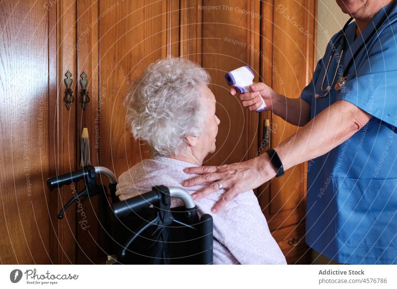 Gesichtslose Krankenschwester misst die Temperatur einer älteren behinderten Frau Krankenpfleger gealtert Sanitäter messen Thermometer Rollstuhl deaktivieren