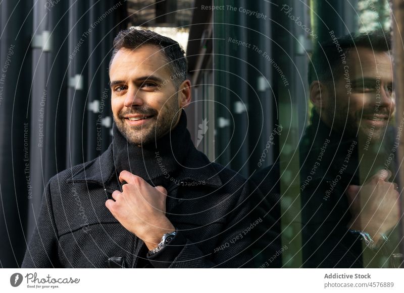 Mann steht neben schwarzem Glas eines modernen Gebäudes Straße selbstbewusst Mantel urban trendy männlich Lächeln Stil Outfit besinnlich Reflexion & Spiegelung