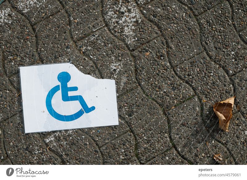 Ein zerrissenes und nasses Behindertenschild auf dem Boden Ableismus Zugang umgänglich Asphalt behindertenparkplatz blau Konzept Behinderung deaktiviert Deutsch