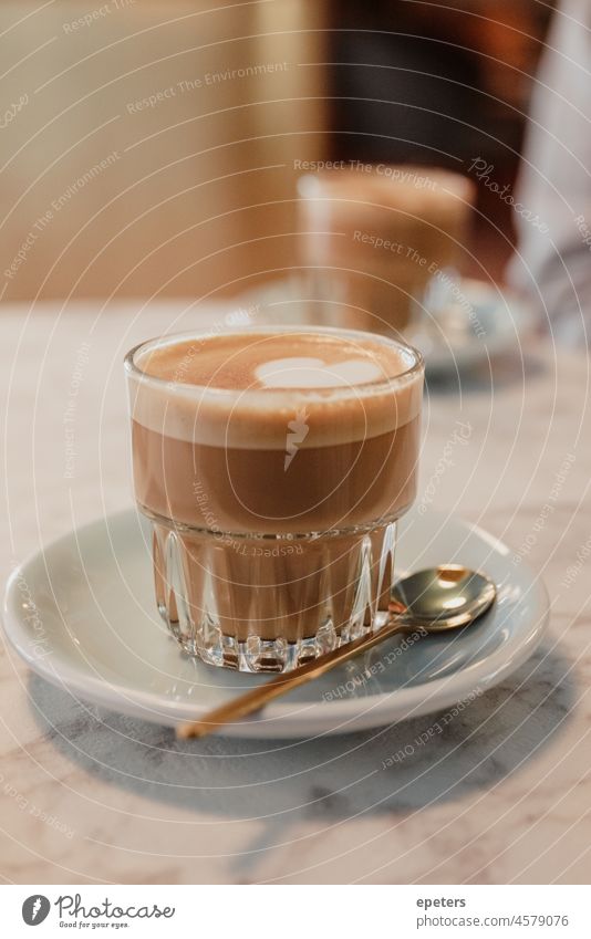 Glastasse mit Milchschaum-Kaffeegetränk auf einer Untertasse auf einem Tisch Aroma Hintergrund Getränk Frühstück braun Café Koffein Cappuccino Sahne Tasse