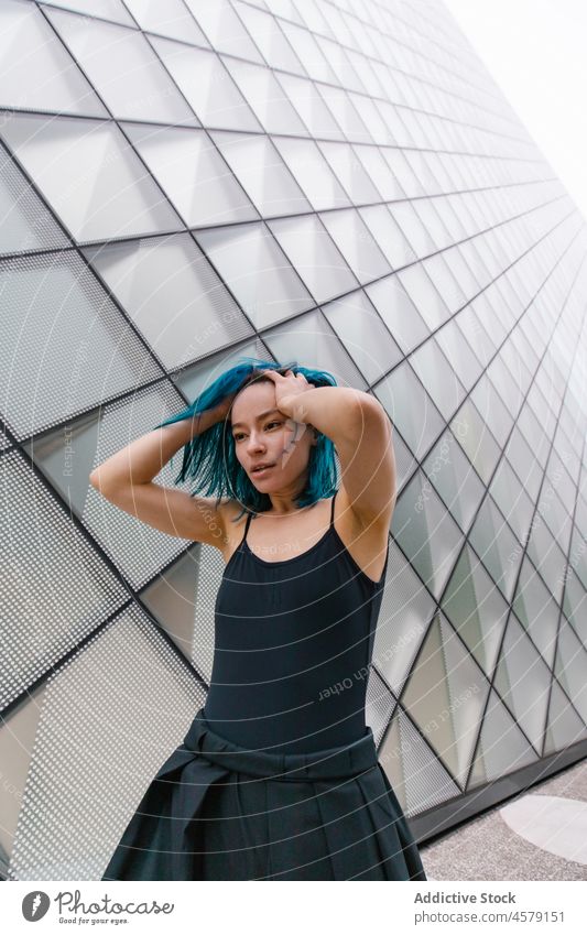 Frau mit blauem Haar steht an der Wand eines modernen Gebäudes Vorschein Zeitgenosse Porträt urban Wolkenkratzer trendy Straße Großstadt Outfit Stil Struktur