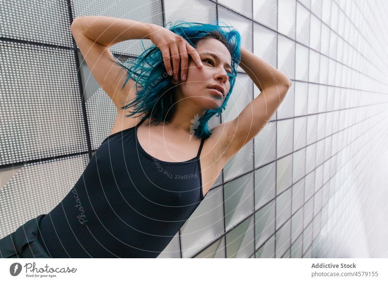 Frau mit blauem Haar steht an der Wand eines modernen Gebäudes Vorschein Zeitgenosse Porträt urban Wolkenkratzer trendy Straße Großstadt Outfit Stil Struktur