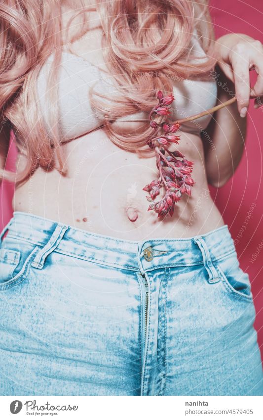 Körperbild einer echten jungen Frau, die Jeans trägt und eine exotische Blume hält positiv wirklich rosa Weiblichkeit Behaarung BH Jeanshose Unterwäsche unten