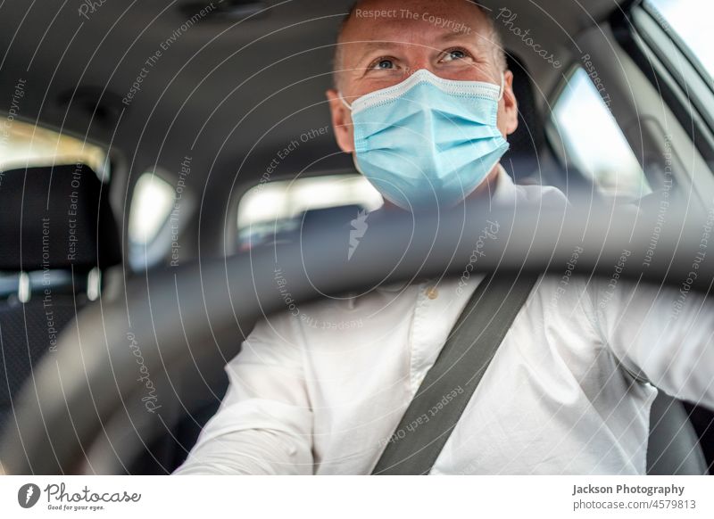 Ein Mann mit einer Schutzmaske fährt ein Auto, das Lenkrad steht im Vordergrund Fahrer Taxi uber Mundschutz Laufwerk Mitfahrgelegenheit behüten Operationsmaske