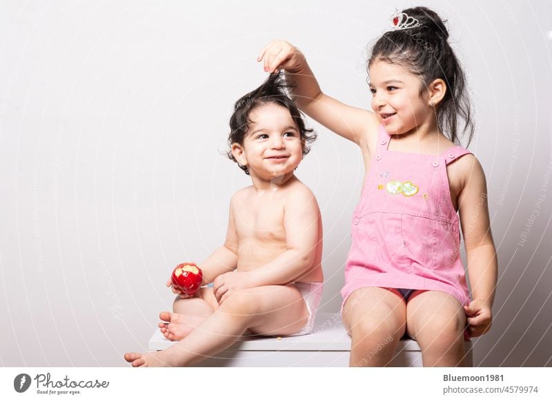 Einjähriges Baby mit Windel neben ihrer Schwester - Freude und fröhliche Momente Familie Spaß Mädchen Kaukasier Essen Apfel Ernährung rot Lebensmittel Sitz eine