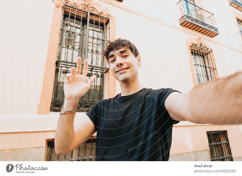 Glücklicher junger Mann mit Hemd, der an einem sonnigen Tag in der Stadt ein Selfie macht und lächelt. Kopieren Raum, gute Stimmung Konzept. Videoanruf grüßt. Reisen Selfie in den europäischen Straßen