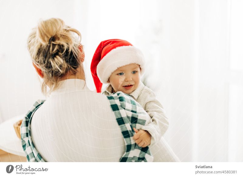 Eine blonde Frau hält ihren kleinen Sohn in einem Weihnachtsmannkostüm im Arm. Das Konzept von Weihnachten und Neujahr Baby Mutter Anzug Beteiligung Familie neu