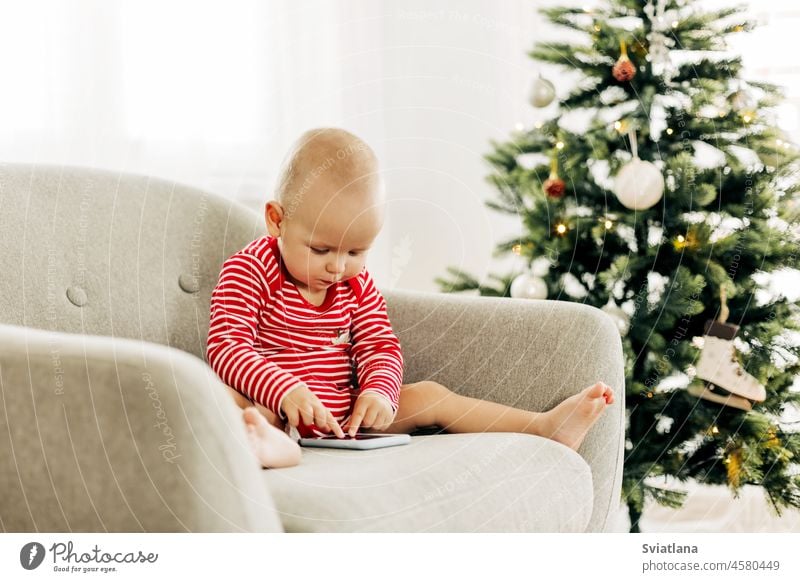 Glücklicher Junge, der auf einem Stuhl neben einem Weihnachtsbaum Cartoons auf einem Smartphone ansieht Weihnachten Baum Baby zuschauend Karikatur Neujahr