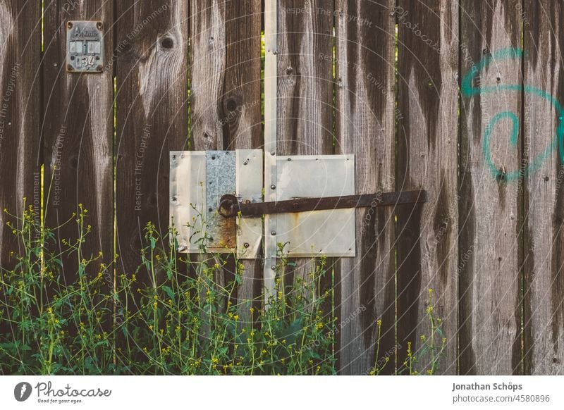 verschlossenes Tor aus Holz und Metall geschlossen Grundstücksgrenze flach Zaun Pflanzen zuwachsen Eingang Tür alt Sicherheit Schloss Strukturen & Formen
