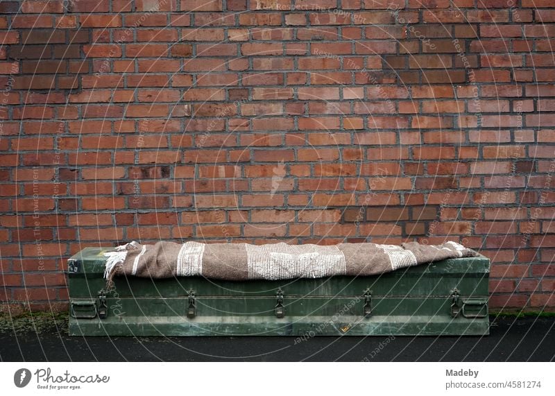 Solide grüne alte Gewehrkiste mit gestreifter brauner Wolldecke als Sitzbank vor rotbrauner alter Fabrikmauer auf einem ehemaligen Fabrikgelände im Stadtviertel Margaretenhütte in Gießen an der Lahn in Hessen