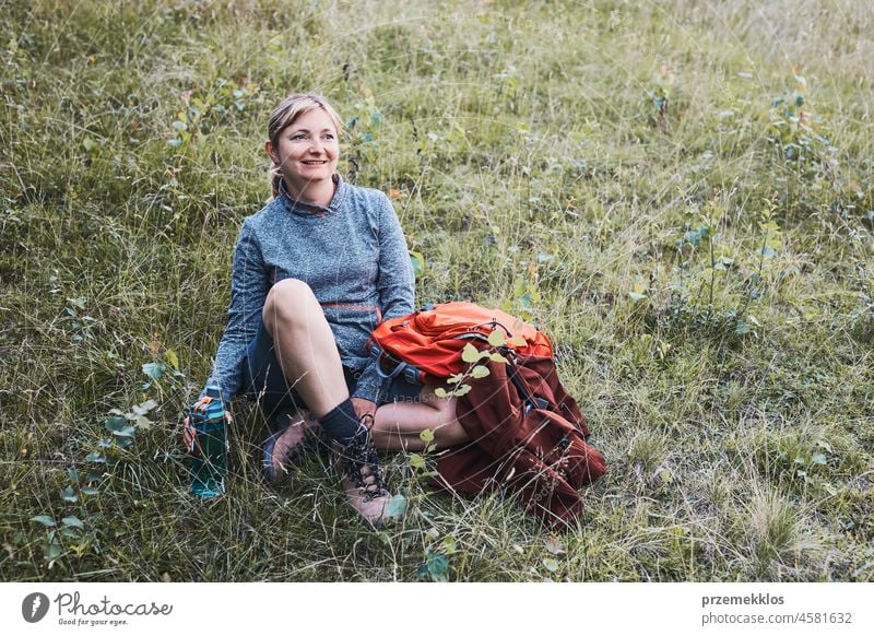 Lächelnde glückliche Frau mit Rucksack, die sich während einer Wanderung in den Bergen im Gras ausruht Sommer Ausflug aktiv Abenteuer Aktivität Spaß reisen