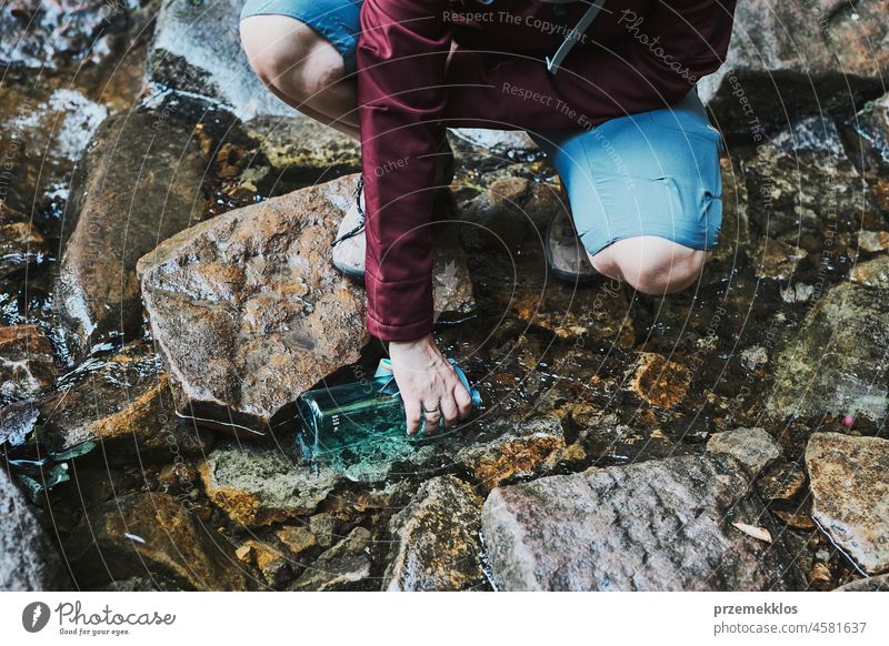 Frau, die beim Trekking in den Bergen reines Wasser aus einem Bergbach in eine Flasche füllt Abenteuer Ausflug reisen wandern durstig strömen Urlaub Reise