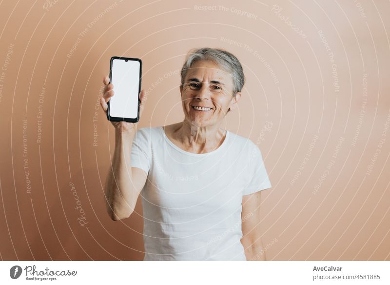 Alte ältere Frau zeigt in die Kamera ein Mobiltelefon Smartphone mit Kopie Raum zu setzen Textanzeige. Ältere Menschen bunten Hintergrund. Weißes T-Shirt Kopie Raum