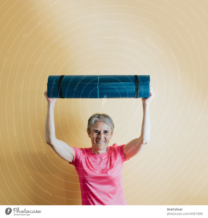 Old Senior weißes Haar Frau hält eine Yoga-Matte mit einem bunten Hintergrund. Fitness alte Menschen Senior Konzept. Gesunde Lebensstile auf ältere Frau zur Bekämpfung der Arthritis