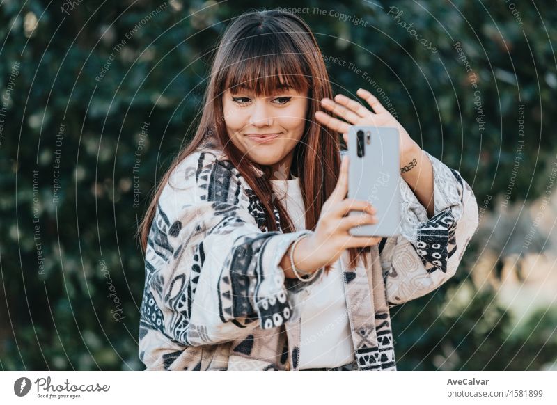 Junge Streamer kaukasischen Mädchen außerhalb mit einem Smartphone zu streamen, glücklich und lächelnd Haltung. Junge und moderne trendigen Stil. Herbstliche Jahreszeit. Arbeiten überall, soziale Netzwerke