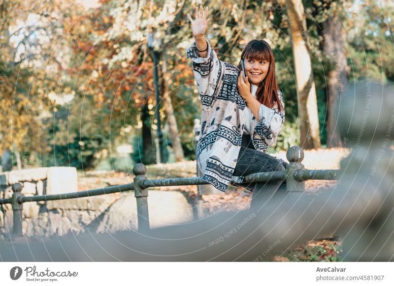 Junge Frau im Park während eines Telefongesprächs, die lächelnd eine gute Nachricht erhält und grüßt, während sie darauf wartet, dass ihre Freunde kommen und sie grüßt, mit Platz für Ihre Werbung oder Ihren Text.