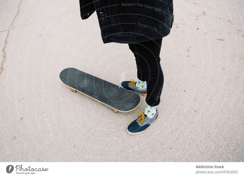 Crop Person in Turnschuhen stehen in der Nähe Skateboard auf Asphalt Straße Skater Großstadt urban Straßenbelag lässig Jeanshose aktiv Aktivität Bein Freizeit