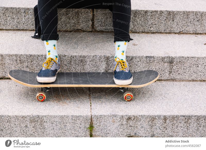 Crop-Skater, der auf den Stufen sitzt und die Beine auf das Skateboard legt Frau Schritt Treppe Treppenhaus Turnschuh trendy Schuhe ruhen urban