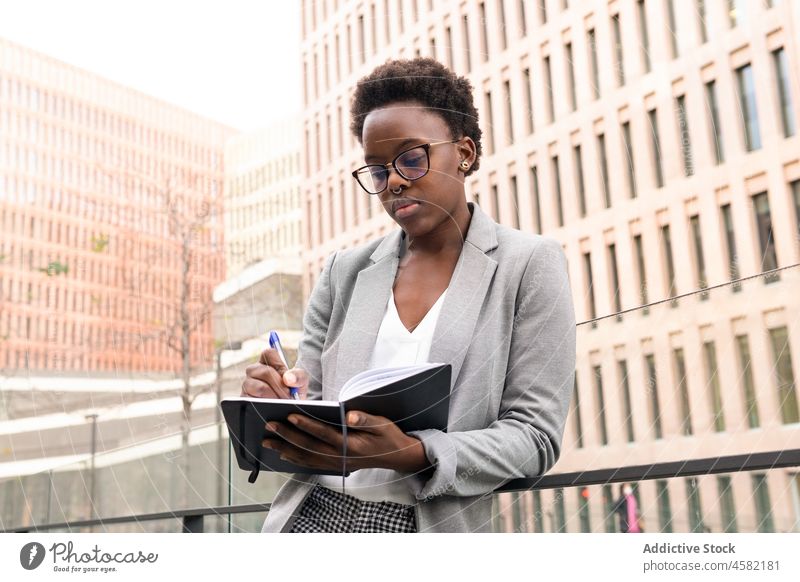 Konzentrierte schwarze Analytikerin, die auf dem Balkon Notizen in einen Planer schreibt Frau Experte Analyst Notebook schreiben zur Kenntnis nehmen Büro