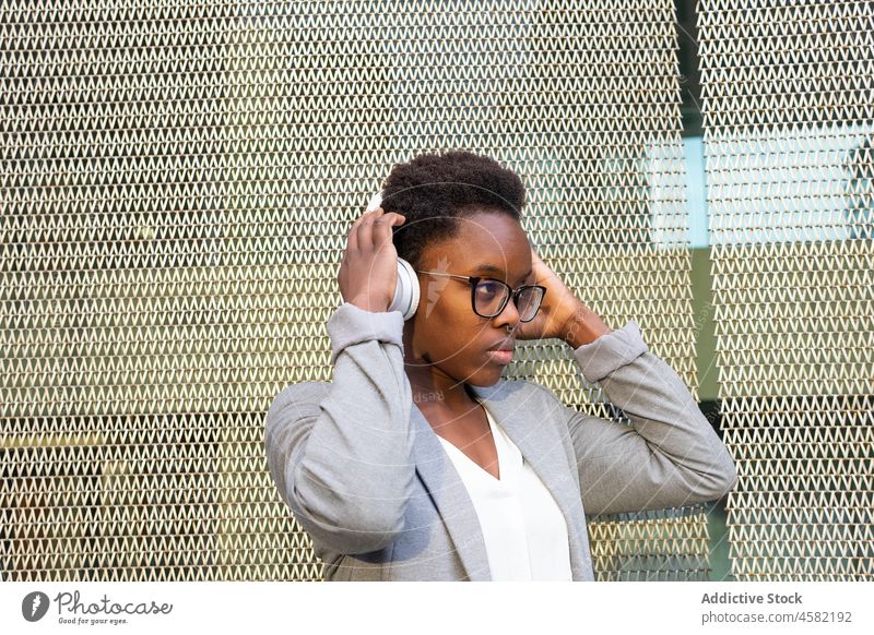 Junge nachdenkliche afroamerikanische Frau, die mit Kopfhörern Musik hört zuhören Raster Gesang Zaun Drahtlos Apparatur Gerät Straße positiv Klang besinnlich