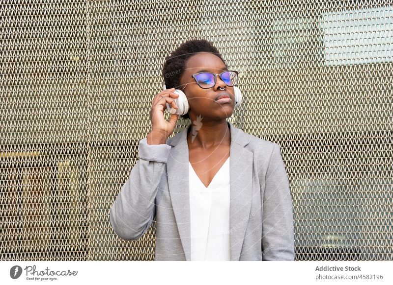 Junge afroamerikanische Frau, die mit Kopfhörern Musik hört zuhören Raster Gesang Zaun Drahtlos Apparatur Gerät Straße positiv Klang Melodie meloman Audio