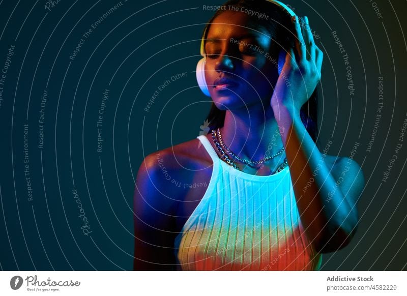 Schwarze brasilianische Frau, die unter Neonlicht Musik hört Stil trendy Atelier fluoreszierend Kopfhörer Gesang meloman ultraviolett schwarz ethnisch