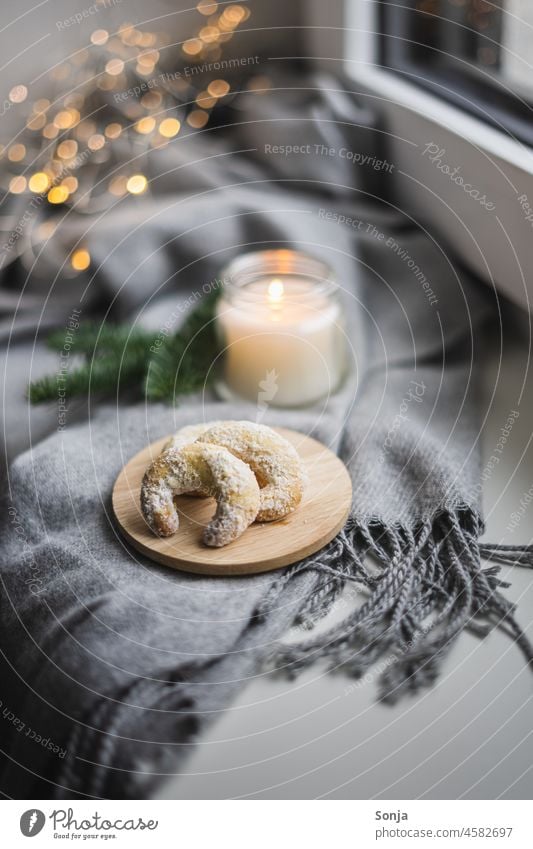 Vanillekipferl auf einem Teller und eine Kerze auf einem Fensterbrett. Weihnachten & Advent Stillleben Hygge hausgemacht Dessert Licht Flamme Kerzenschein