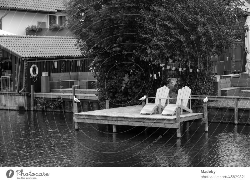 Schöne Liegestühle aus Holz auf einem alten Bootssteg aus Holz am Hafen in Steinhude am Steinhuder Meer bei Wunstorf im Landkreis Hannover, fotografiert in neorealistischem Schwarzweiß