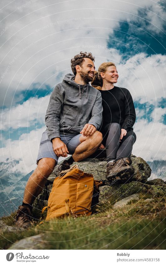 junges Paar auf einem Berggipfel Gipfel Stein Himmel Wolken Wandern Rast Pause Ausblick Bergblick Aussicht lächeln freundlich sportlich Bewegung Urlaub Berge