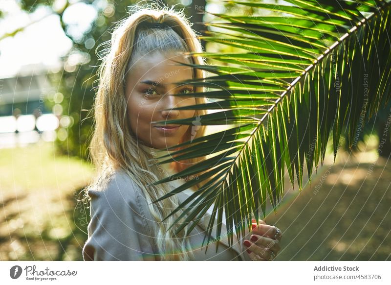 Junge Frau in der Nähe von grünen Palmenblatt in sonnigen Tag Park Porträt Handfläche Baum charmant tropisch Natur blond sich[Akk] entspannen Garten ruhen
