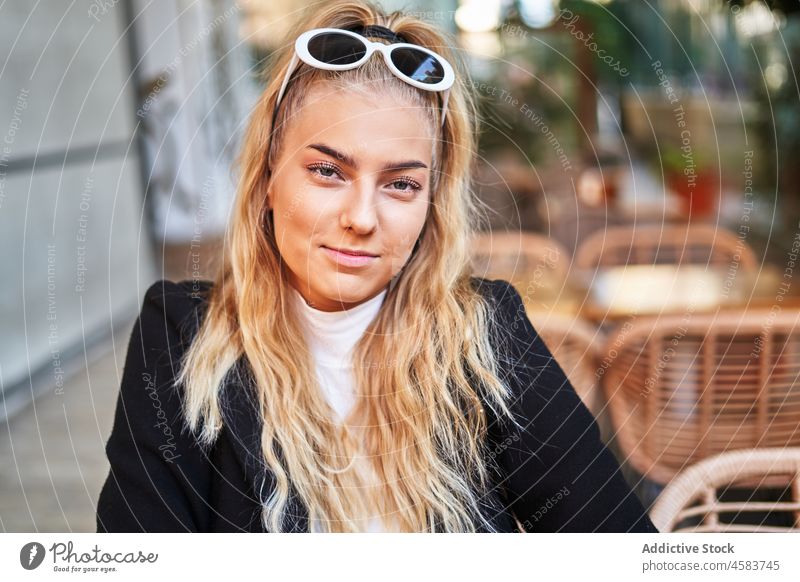 Positive Frau sitzt am Tisch auf der Terrasse eines Cafés Veranda Porträt sich[Akk] entspannen trendy blond positiv Kälte Jacke Inhalt Sonnenbrille Kantine