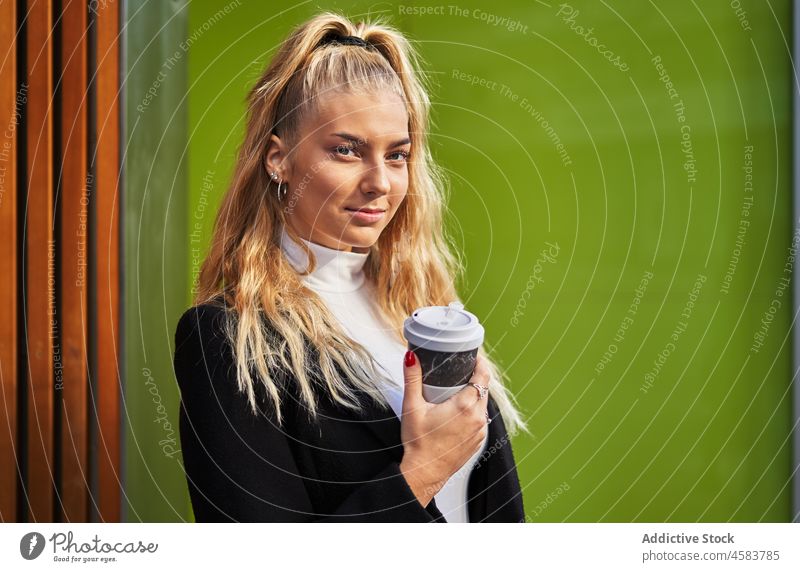 Junge blonde Frau mit Kaffee zum Mitnehmen und Rucksack Imbissbude Stil träumen ruhen Leder urban Getränk verträumt Mantel hölzern Windstille Wand Pappbecher