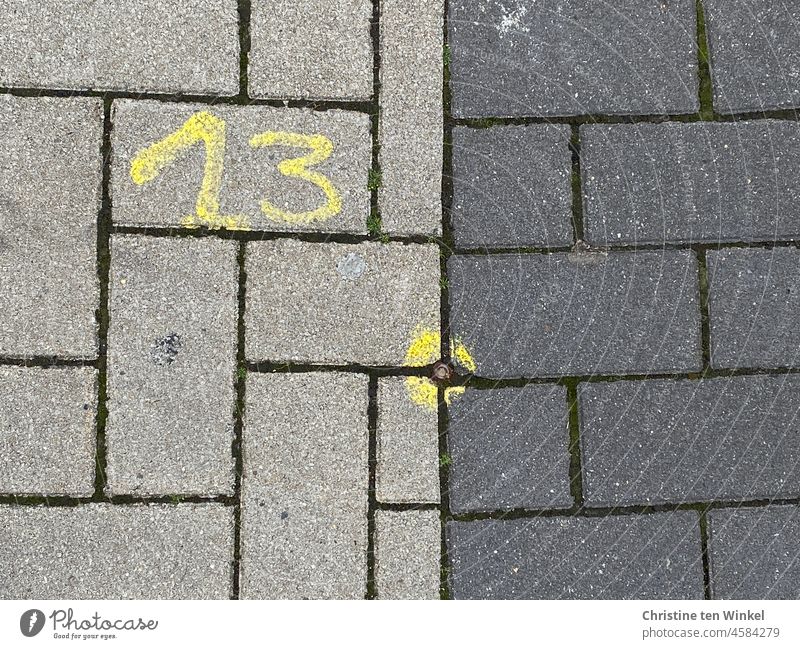 Eine gelbe 13 und eine gelbe Markierung auf hellgrauen und dunkelgrauen Pflastersteinen Zahl Ziffern & Zahlen Dreizehn Kreis Punkt Gehweg Gehwegpflaster