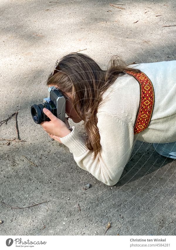 Eine junge Frau kniet auf dem Gehweg und fotografiert mit einer alten analogen Kamera fotografin Junge Frau fotografieren analoge Kamera vintage alte Kamera