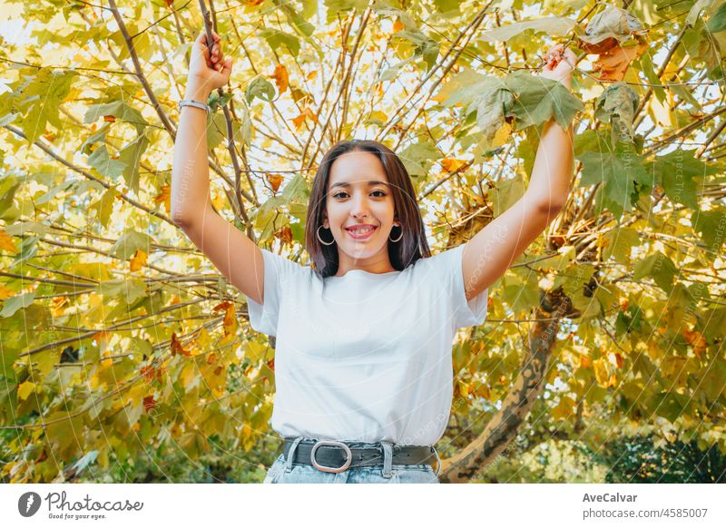 Afrikanisches arabisches junges Mädchen zwischen grünen Blättern lächelnd. Pointing Copy Raum für Text und fügt. Trendige Kleidung, Jeans und weißes T-Shirt modernes Styling. Soziale Netzwerke
